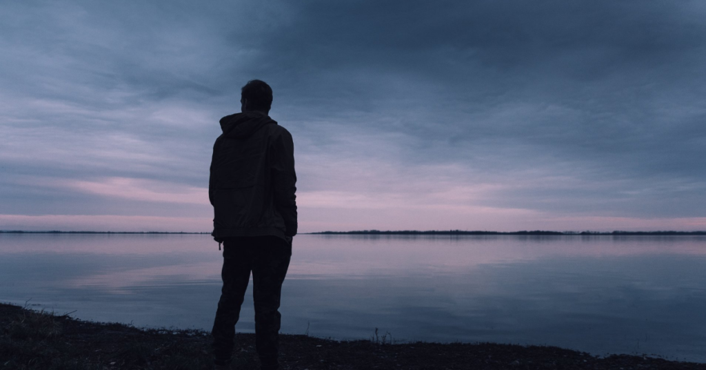 A person stands alone against a shore on a gray, overcast day.